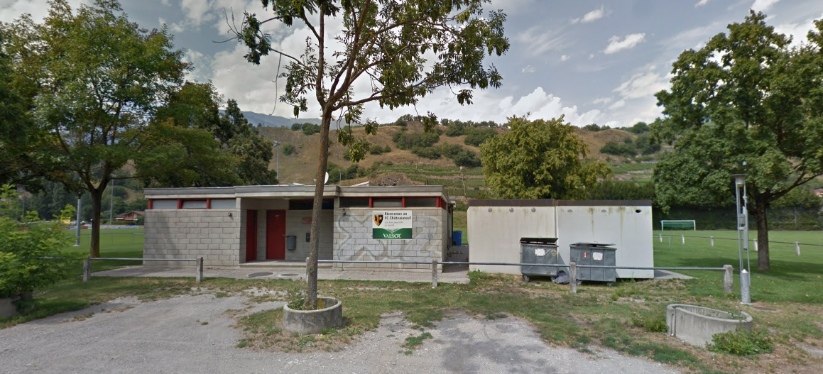 Un petit bâtiment est situé au milieu d'un champ entouré d'arbres.