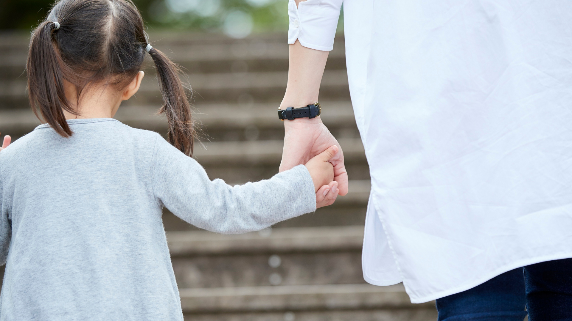 Child holding an adult’s hand while walking up outdoor steps