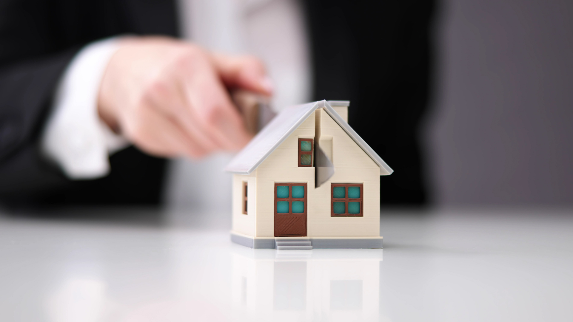 Hand placing a small model house on a white surface