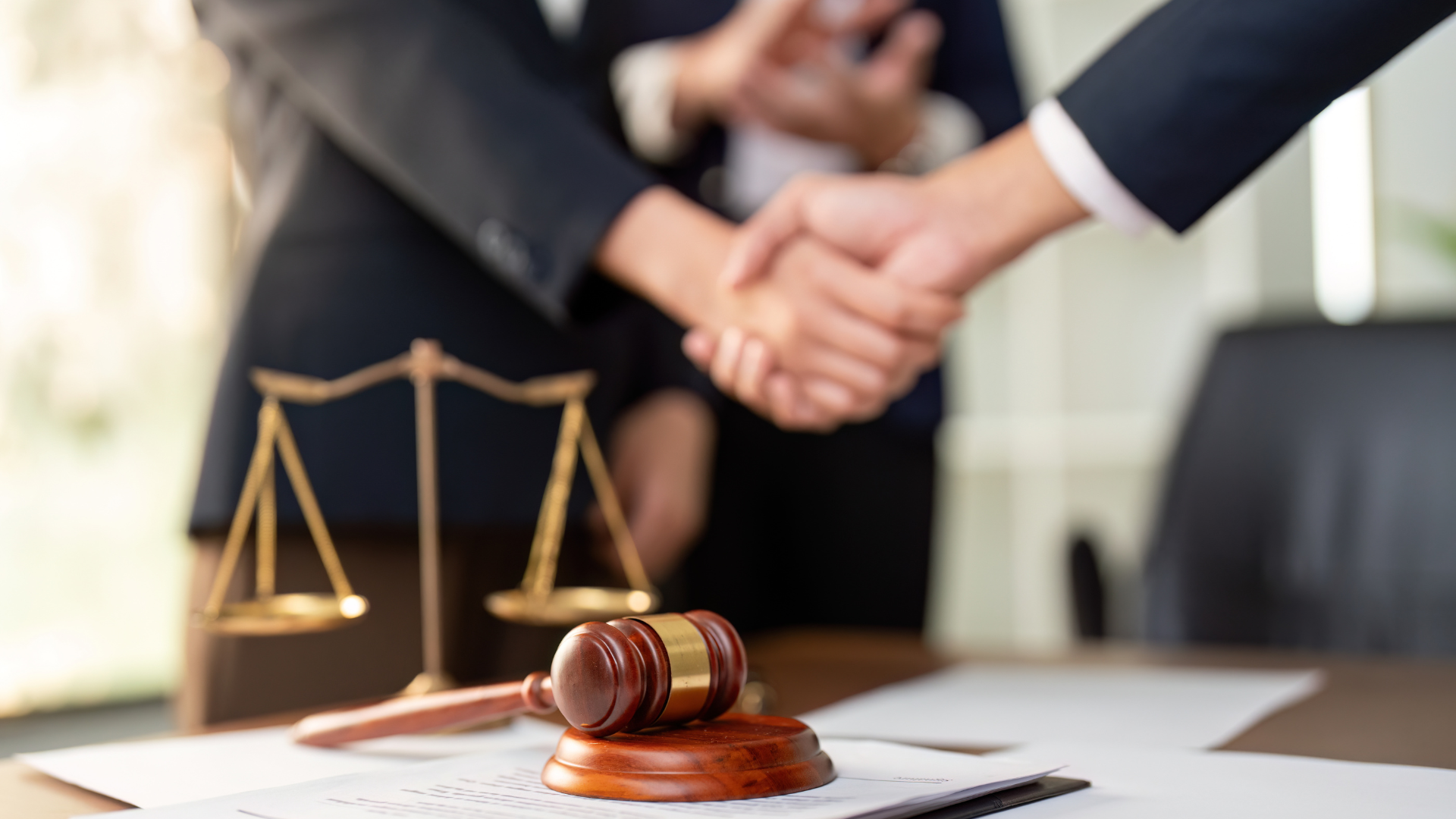 Lawyer’s handshake beside gavel and scales of justice on a desk