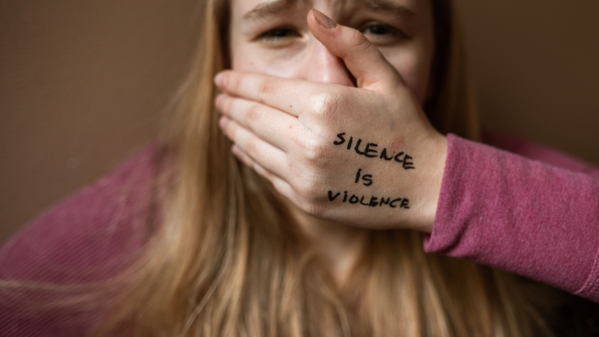 Hand covering a woman’s mouth with “silence is violence” written on the hand