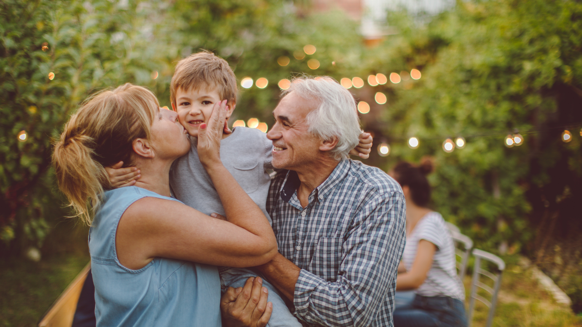 Woman and older man lifting a smiling child in a sunlit garden