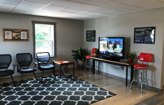 Waiting room with chairs, TV, plants, and a geometric rug  | Gateway Automotive Inc.
