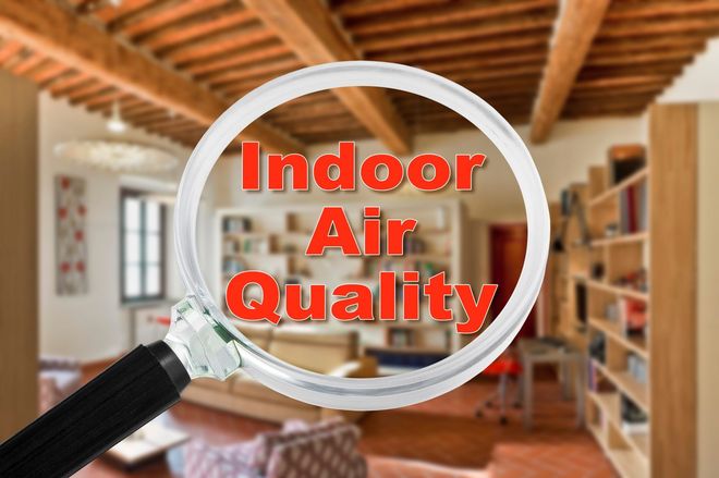 Magnifying glass over red “Indoor Air Quality” text in a cozy room with bookshelves and wooden ceiling beams