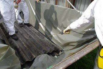 Workers in white suits spray a tarp-covered, corrugated roof on a truck bed