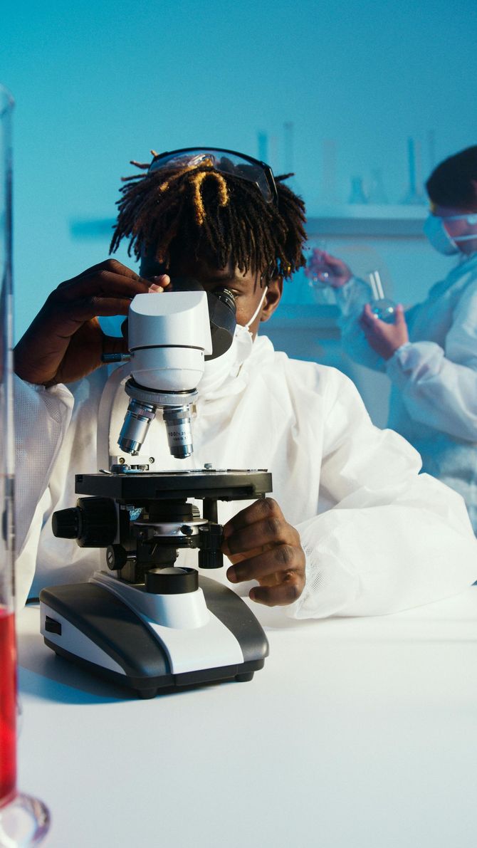 Scientist in red jacket holding a sample beside a microscope in a lab workspace