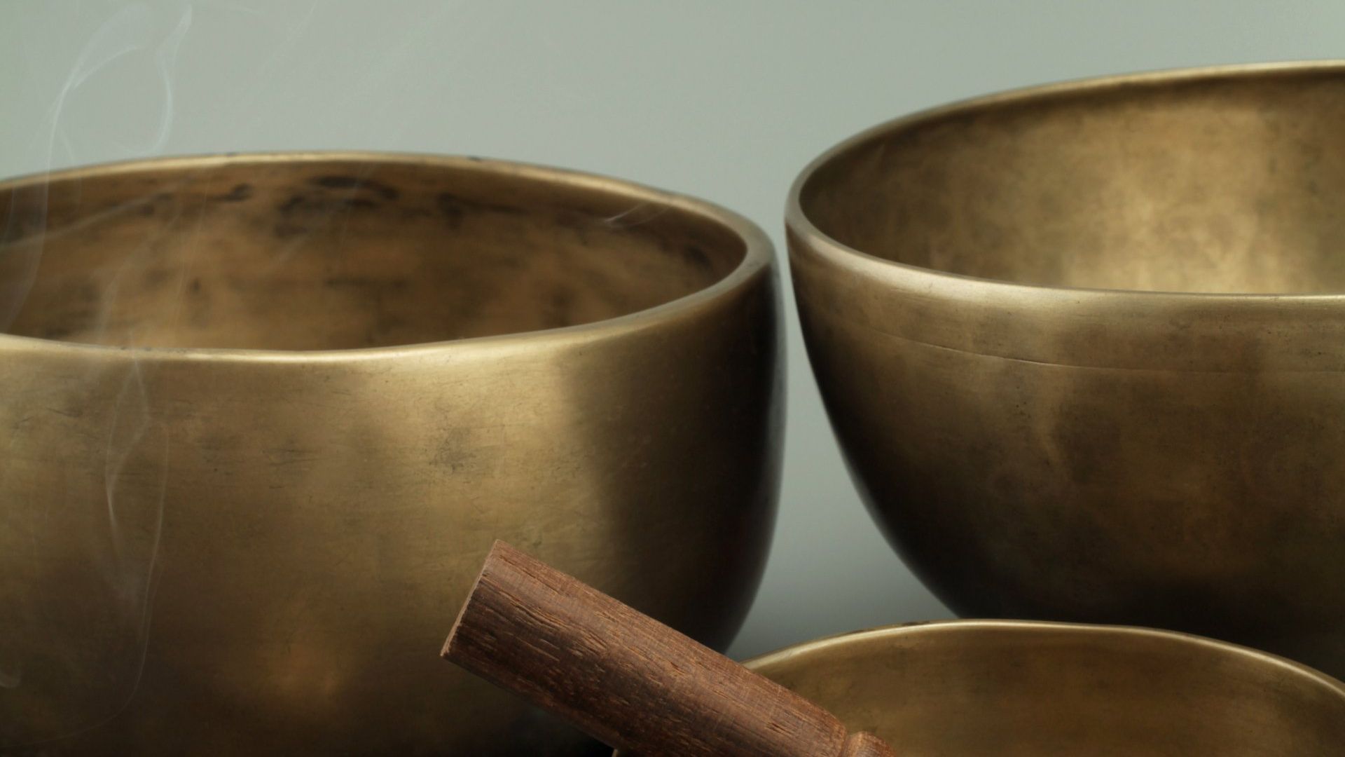 Three brass bowls with wooden handles are sitting next to each other on a table.