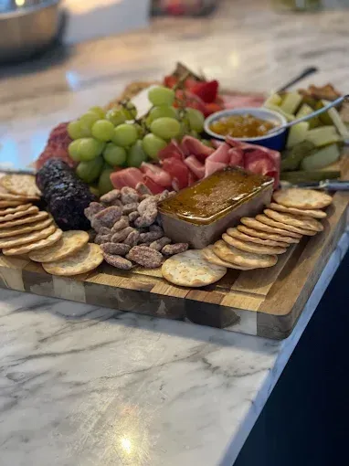 Charcuterie board with grapes, cheese, nuts, crackers, and meat on a wooden board, marble surface.
