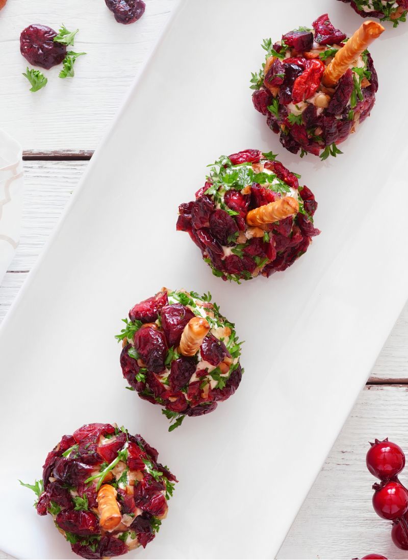 Cranberry and cheese balls lined up on a white platter, garnished with parsley and a pretzel stick.