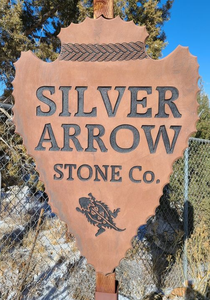 Rust-colored sign reading “SILVER ARROW STONE CO.” among trees and blue sky