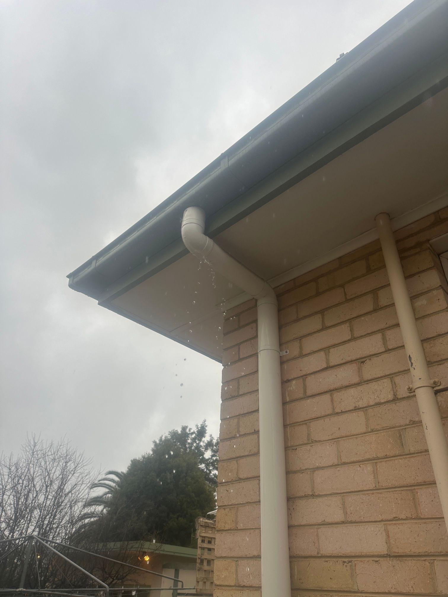 Rainwater pouring from a white gutter into a downspout against a brick wall.