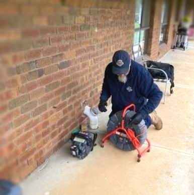 Plumber inspecting pipes outside a brick building using inspection equipment.