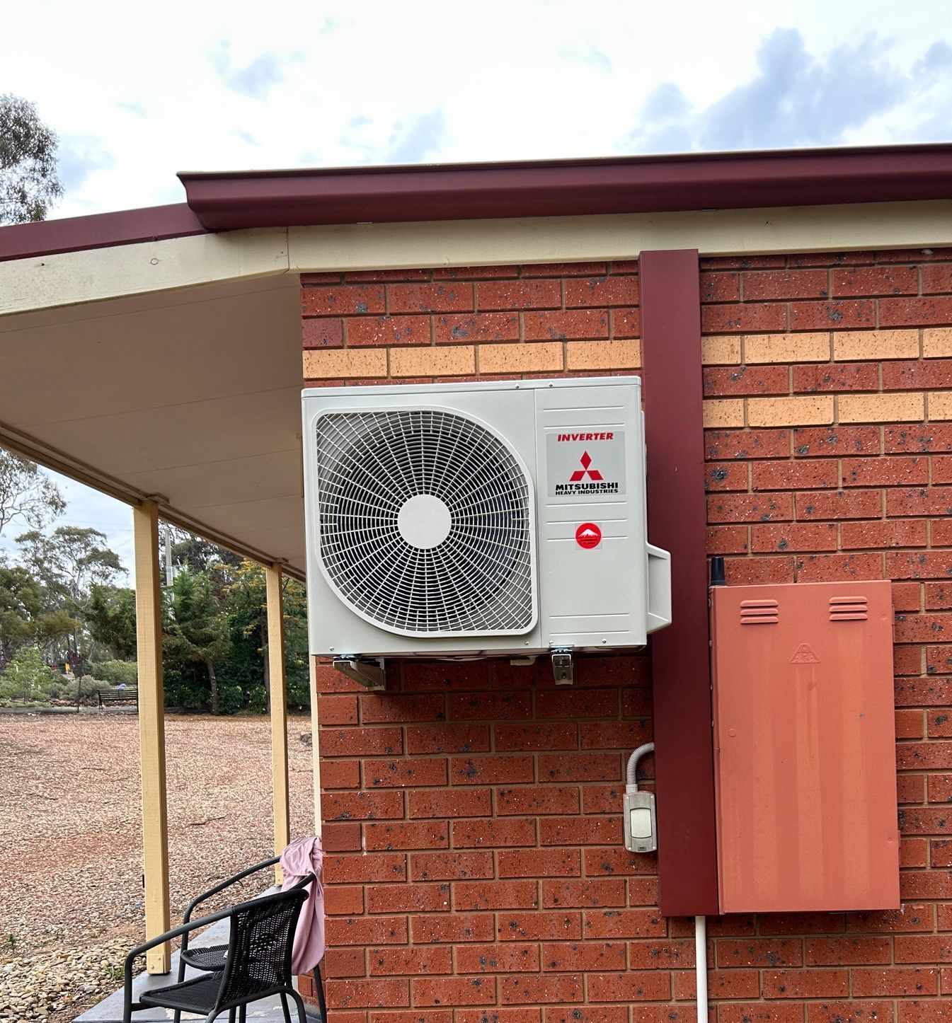 Mitsubishi air conditioning unit on a red brick wall, next to a red metal box.