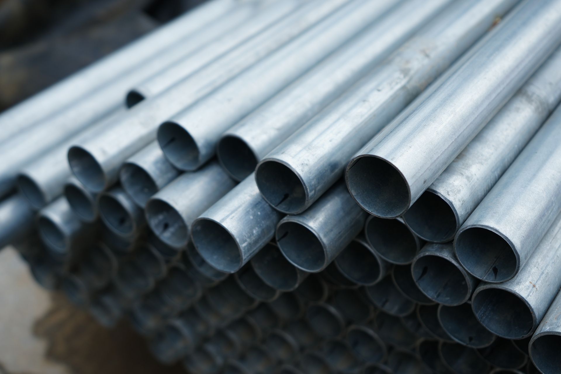 Stack of galvanized steel pipes arranged in rows at construction site storage area.