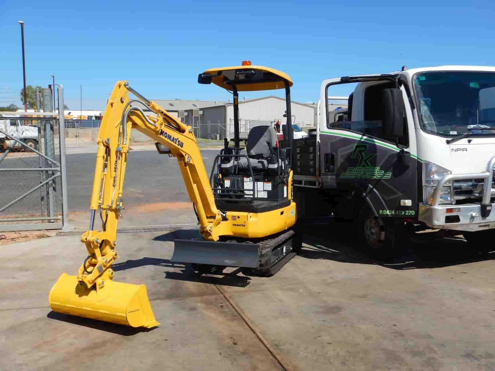 A Small Yellow Excavator is Parked Next to a White Truck — RK Diesel Services in Ciccone, NT