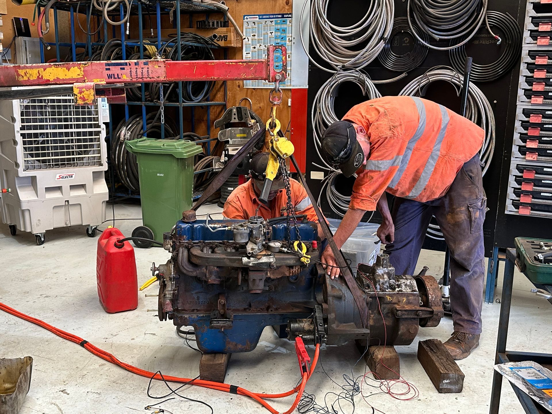 Two mechanics in orange workwear, inspecting an engine in a workshop setting. — RK Diesel Services in Ciccone, NT