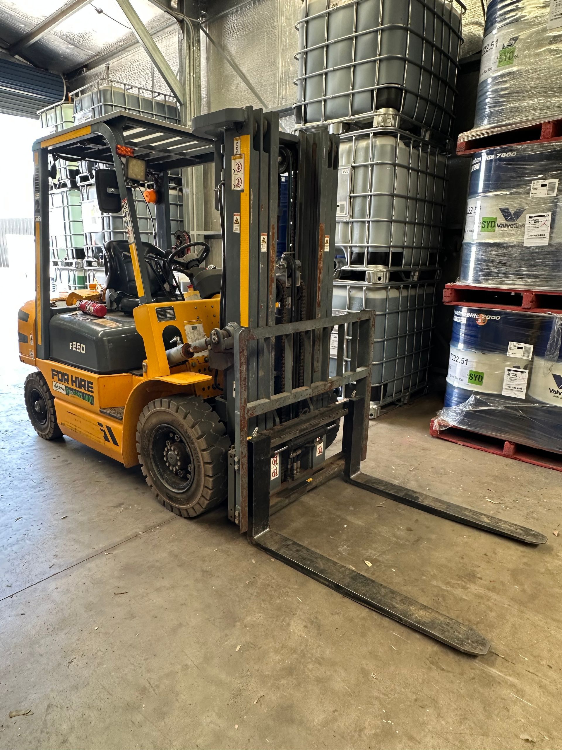 Yellow forklift in a warehouse, with stacks of large containers in the background. — RK Diesel Services in Ciccone, NT