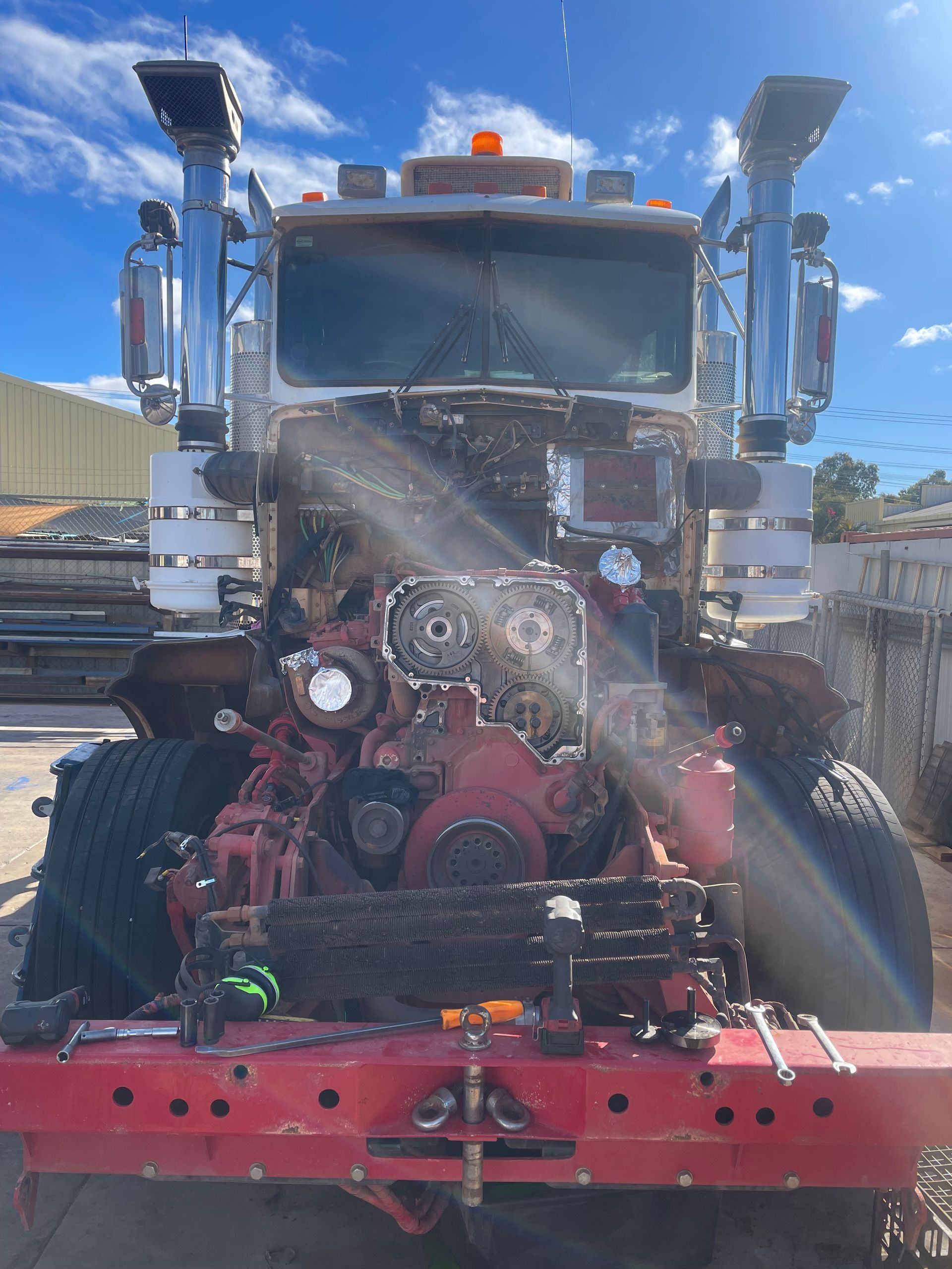 Front of a semi-truck with engine exposed, red frame, chrome exhaust pipes, outdoor setting. — RK Diesel Services in Ciccone, NT
