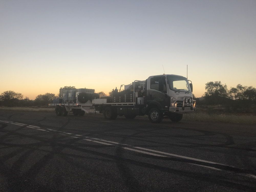 Two Trucks Are Parked on the Side of the Road at Sunset — RK Diesel Services in Ciccone, NT