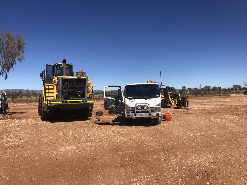 A Truck and a Bulldozer Are Parked in a Dirt Field — RK Diesel Services in Ciccone, NT