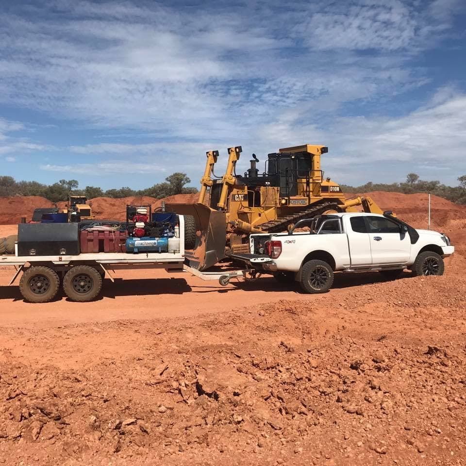 A White Truck is Towing a Bulldozer on a Trailer — RK Diesel Services in Ciccone, NT
