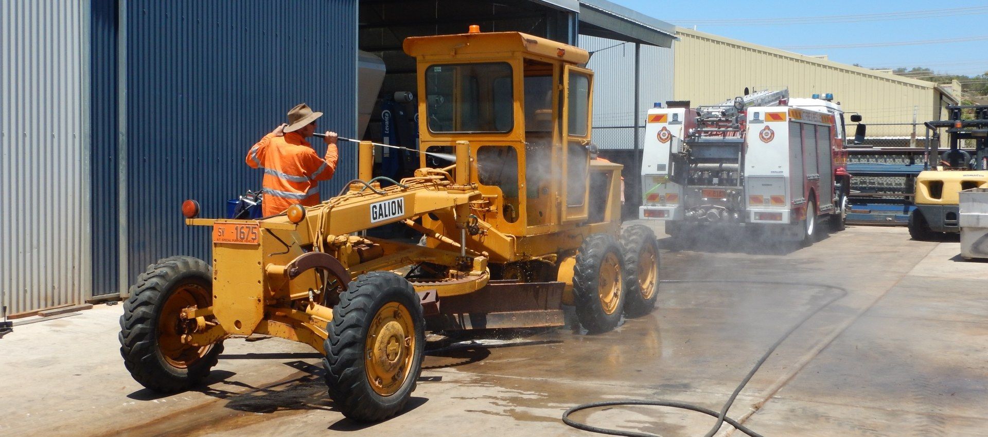 A man is washing a yellow tractor in a parking lot. — RK Diesel Services in Ciccone, NT