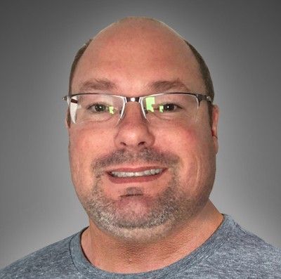 A bald man with glasses and a beard is smiling for the camera.
