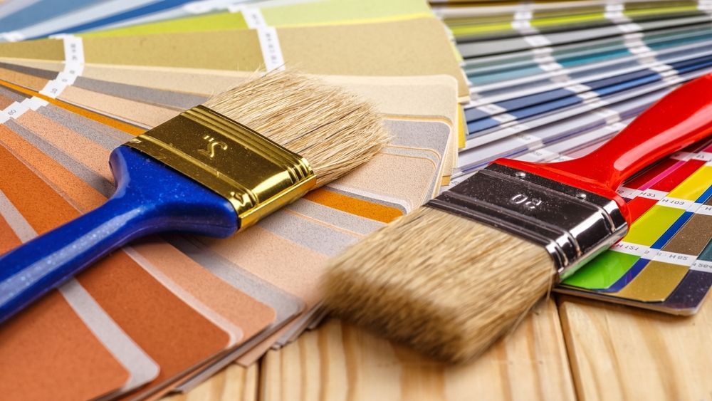 Paintbrushes rest on colorful paint swatches on wood surface.