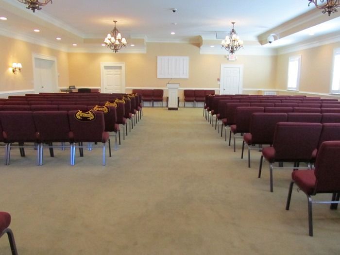 An interior view of a quiet, empty auditorium with rows of burgundy chairs facing a central podium and a white wall board.