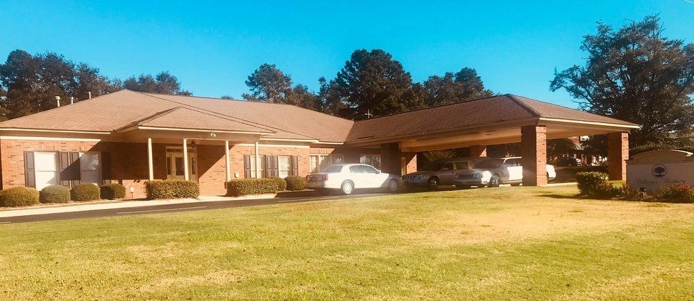 A single-story, brick building with a large entrance portico, situated on a lawn under a clear blue sky.
