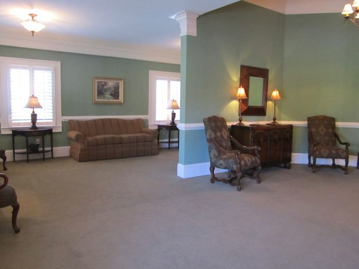 A seating area with sage green walls, a brown sofa, two armchairs, side tables, lamps, and a mirror on the wall.