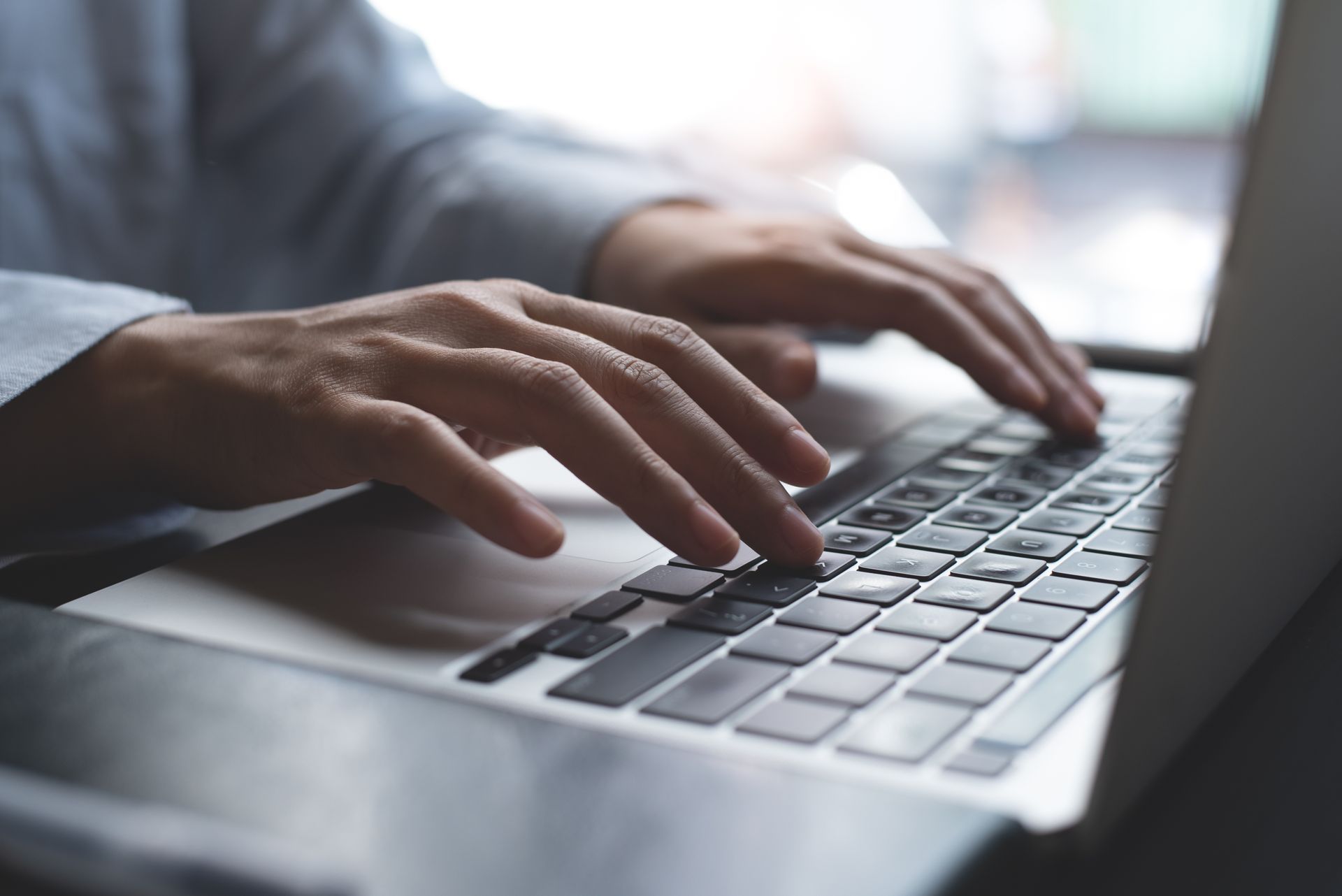 Close-up of hands typing on a laptop keyboard in a workspace.