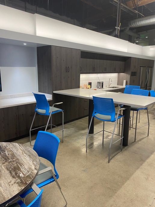 Office break room with dark cabinets, gray counter, and blue bar stools.