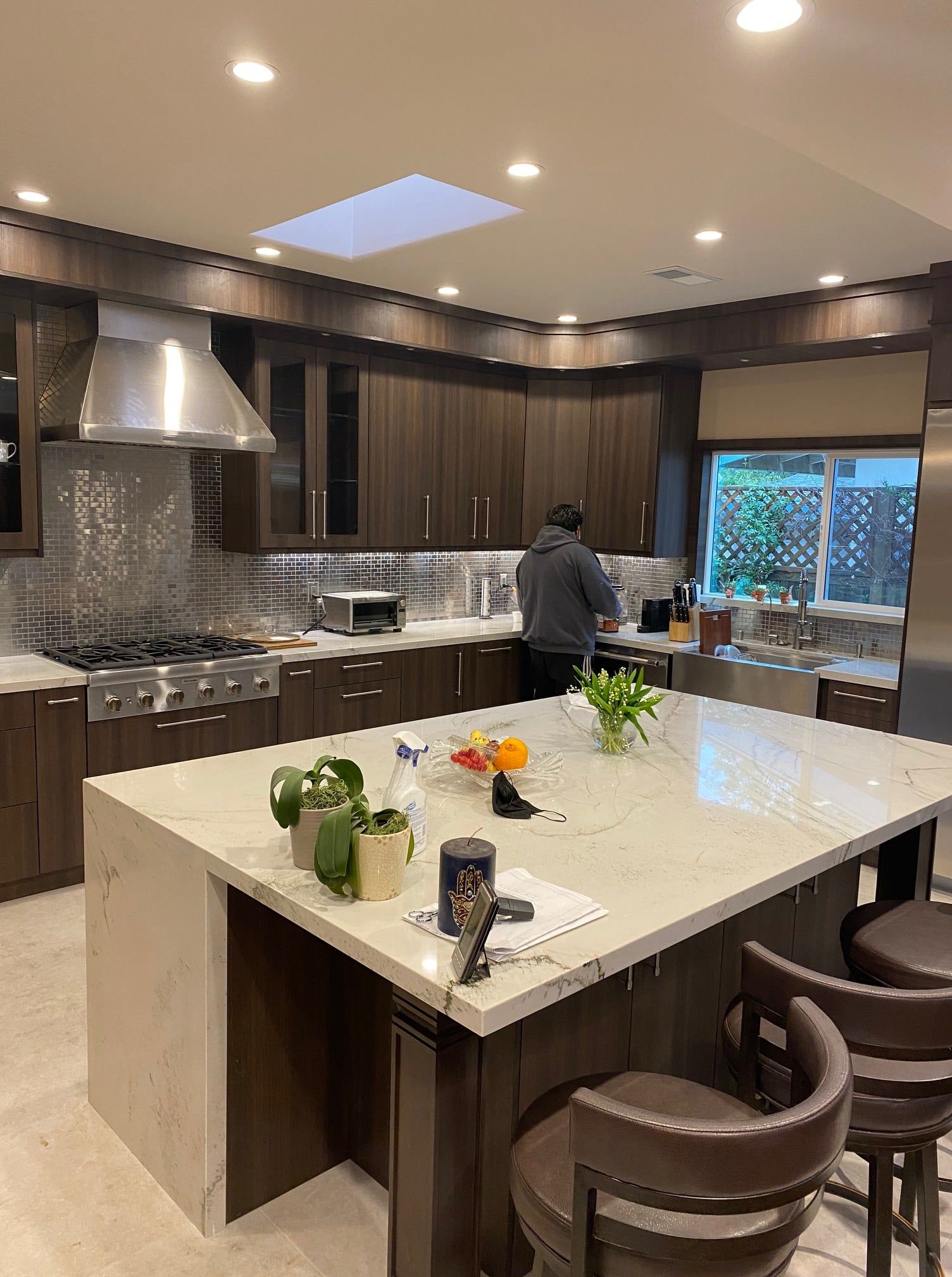Man cooking in a modern kitchen with dark wood cabinets, stainless steel appliances, and a large island.