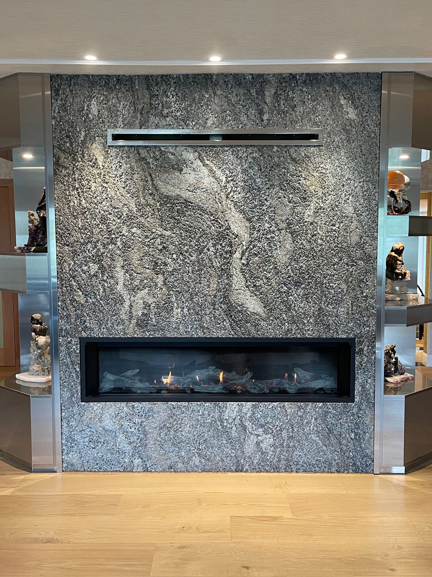 Modern fireplace with black frame against textured gray wall; flanking shelves with décor.
