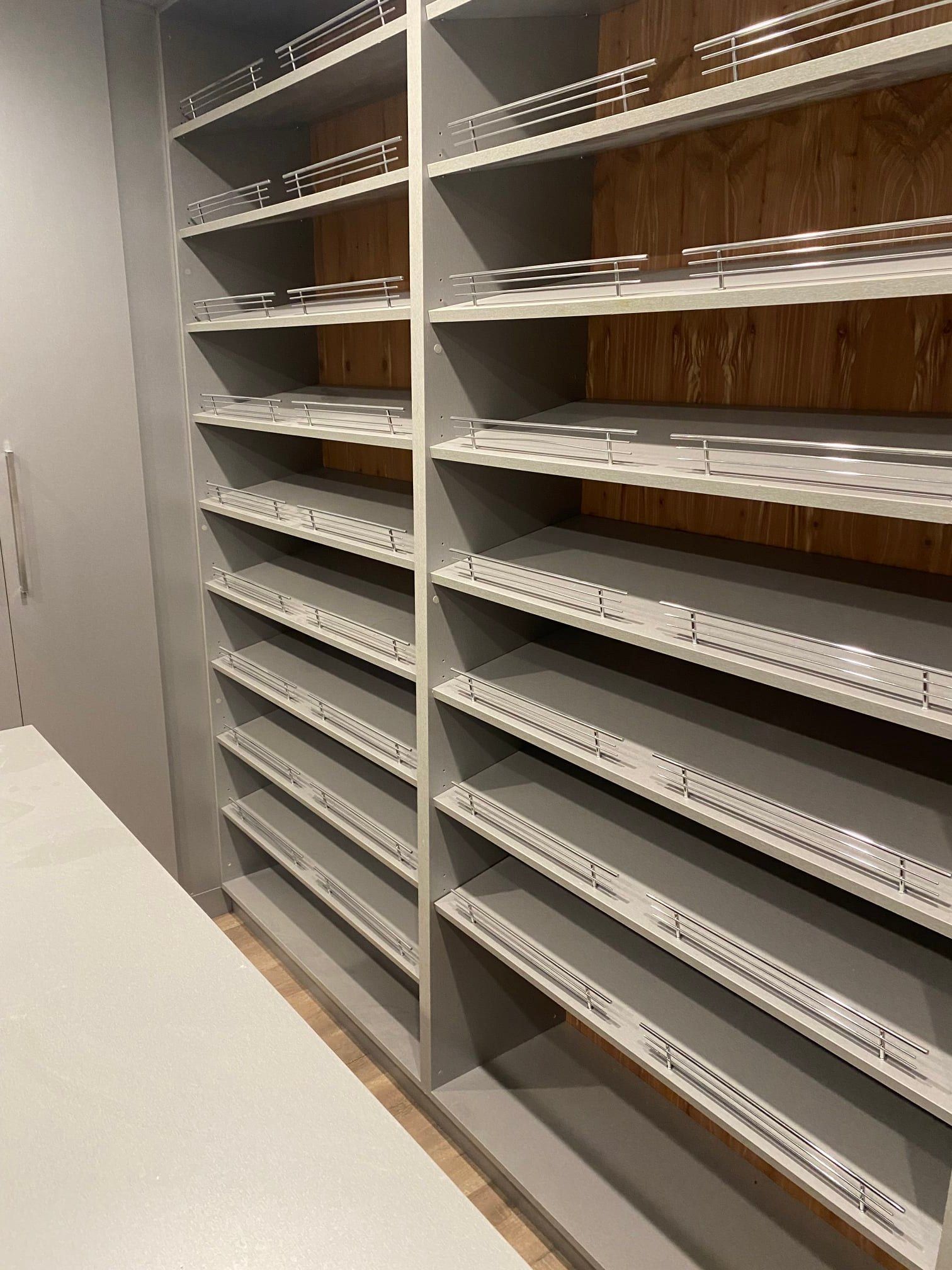 Gray shelving unit with many open shelves, wooden back, on a white floor.