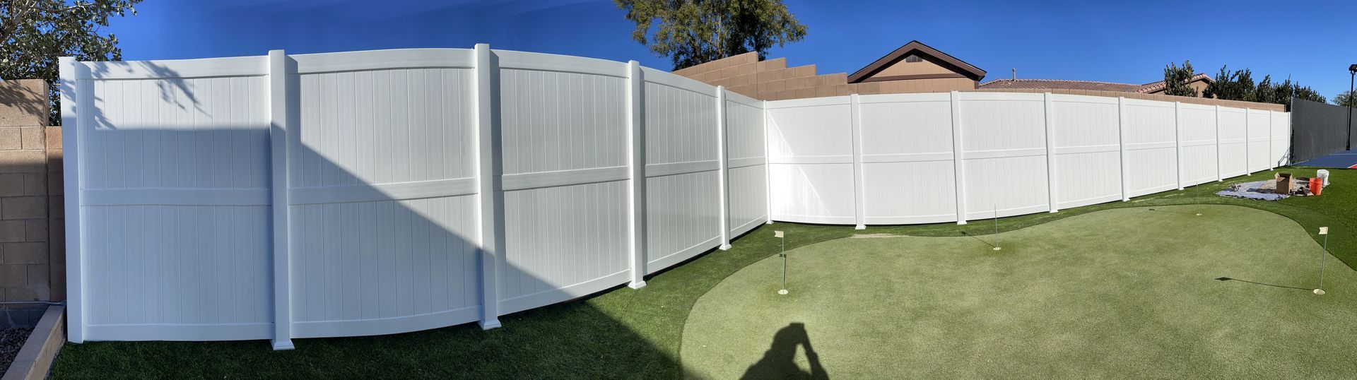 A white fence surrounds a golf course in a backyard.