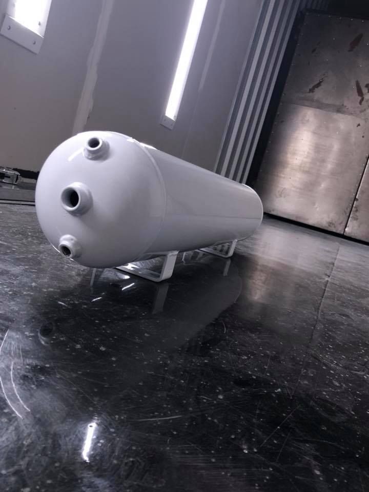 White air tank on a stand in a shiny, dark-floored room with bright overhead lights.