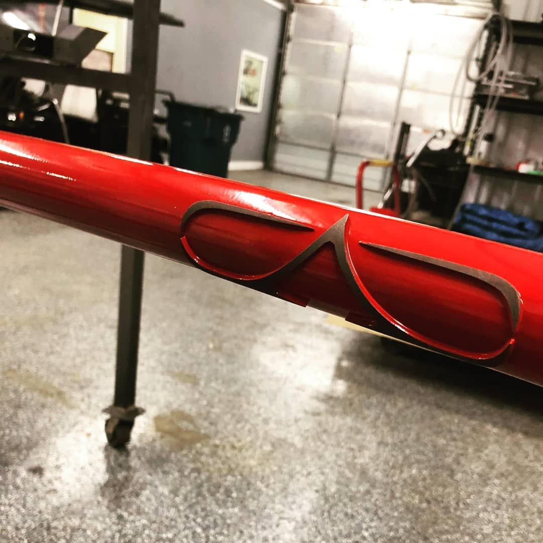 Red metal tube with two brown, stylized wing-shaped cutouts. In a workshop setting.