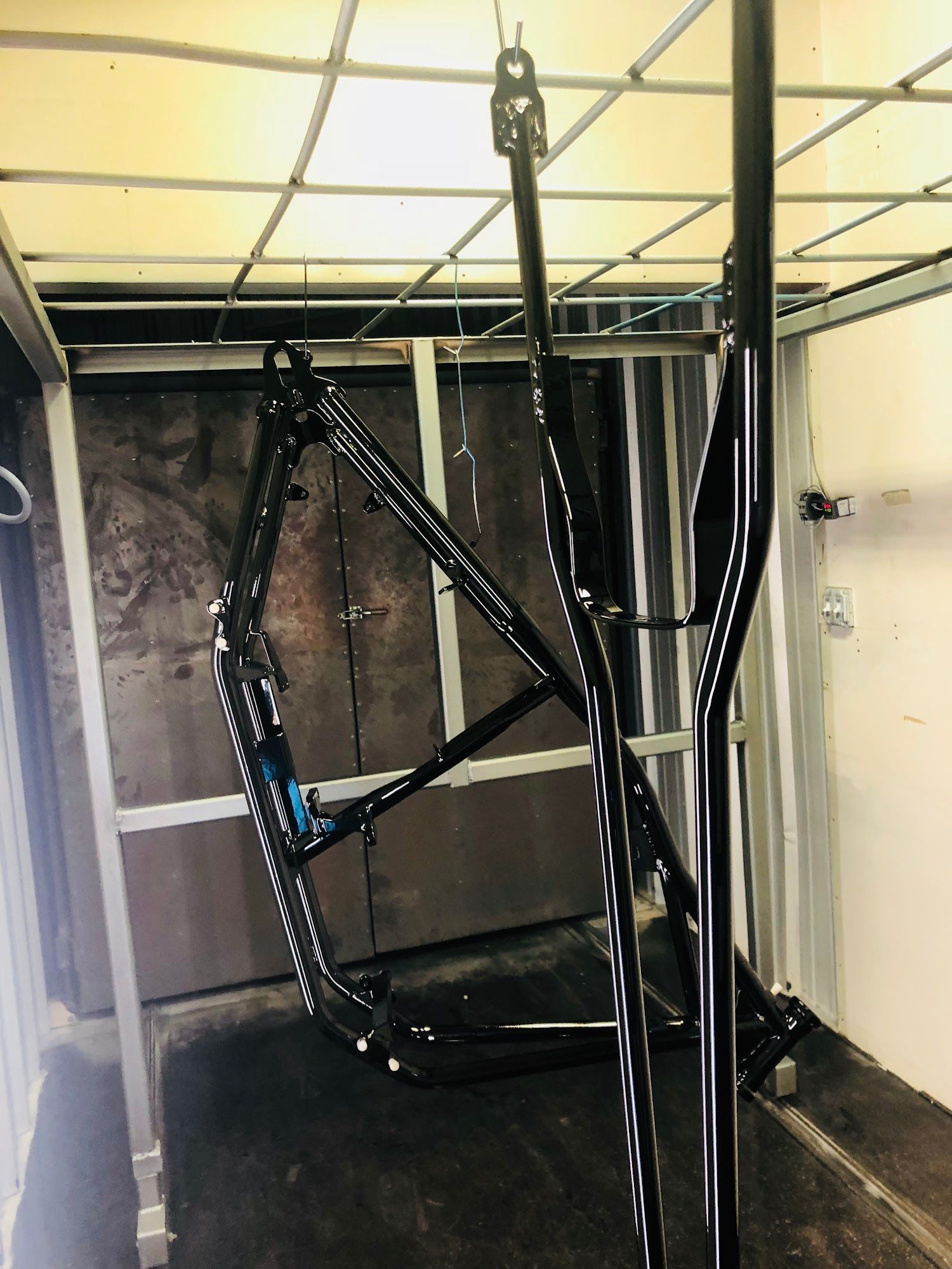 Black bicycle frame suspended in a paint booth.