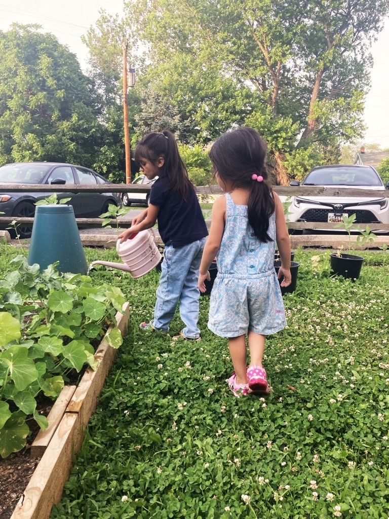 Maria’s two daughters play in AWE’s community garden.