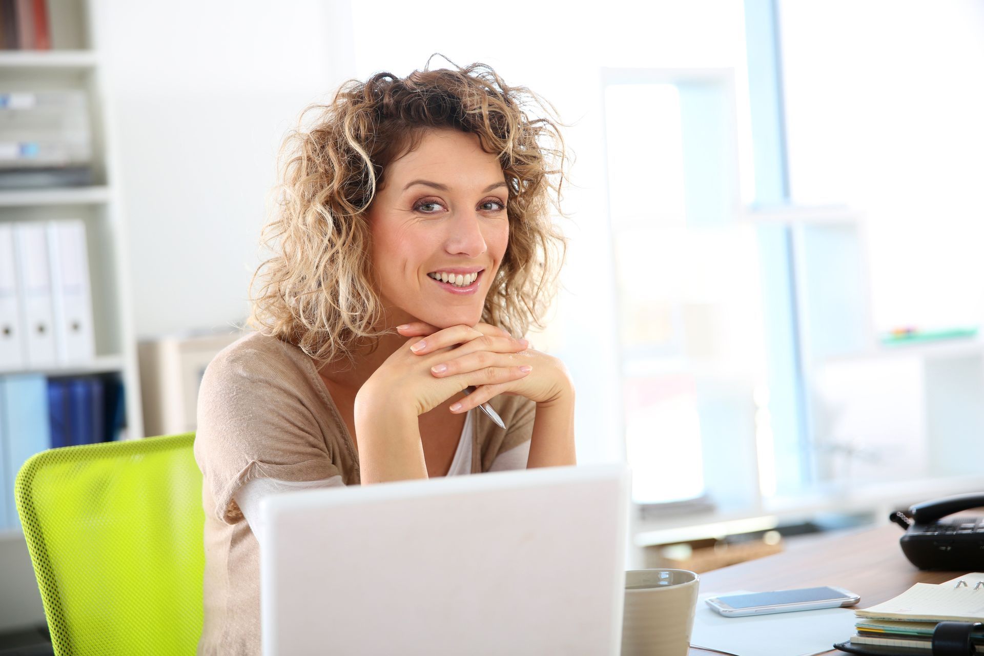 A woman in a green shirt is smiling with her arms crossed.