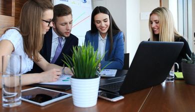 A group of people are sitting around a table looking at a laptop.