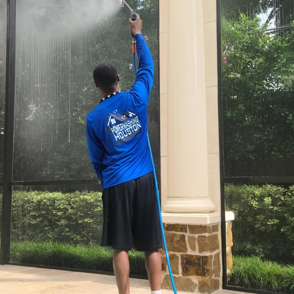 A man in a blue shirt is spraying water on a screened in porch.