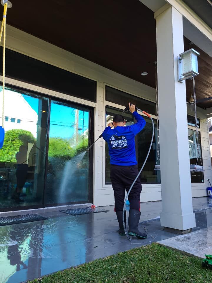 A man in a blue shirt is cleaning a window with a hose.