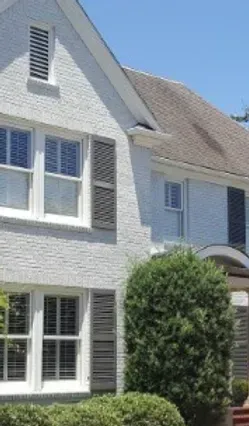 A white house with black shutters on the windows and a brown roof.