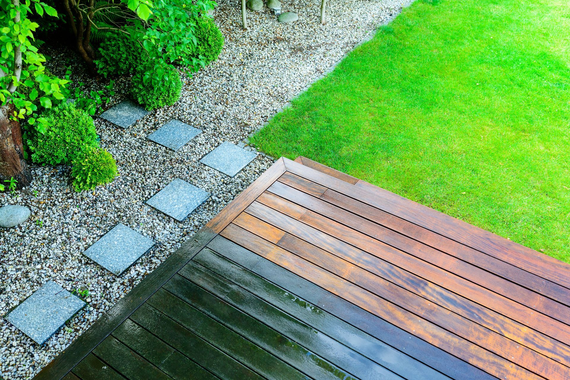A wooden deck in a garden next to a lush green lawn.