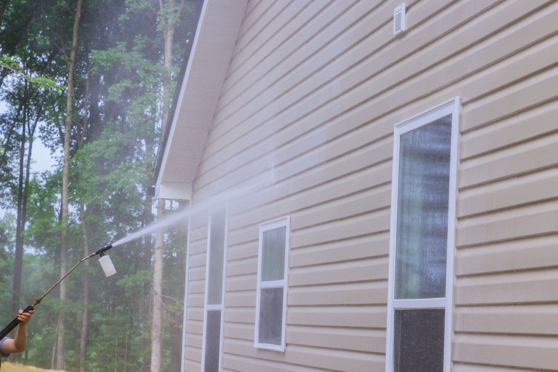 A man is using a high pressure washer to clean the side of a house.