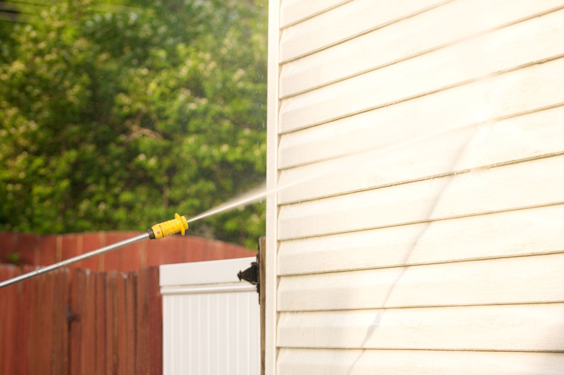 A person is cleaning the side of a house with a pressure washer.