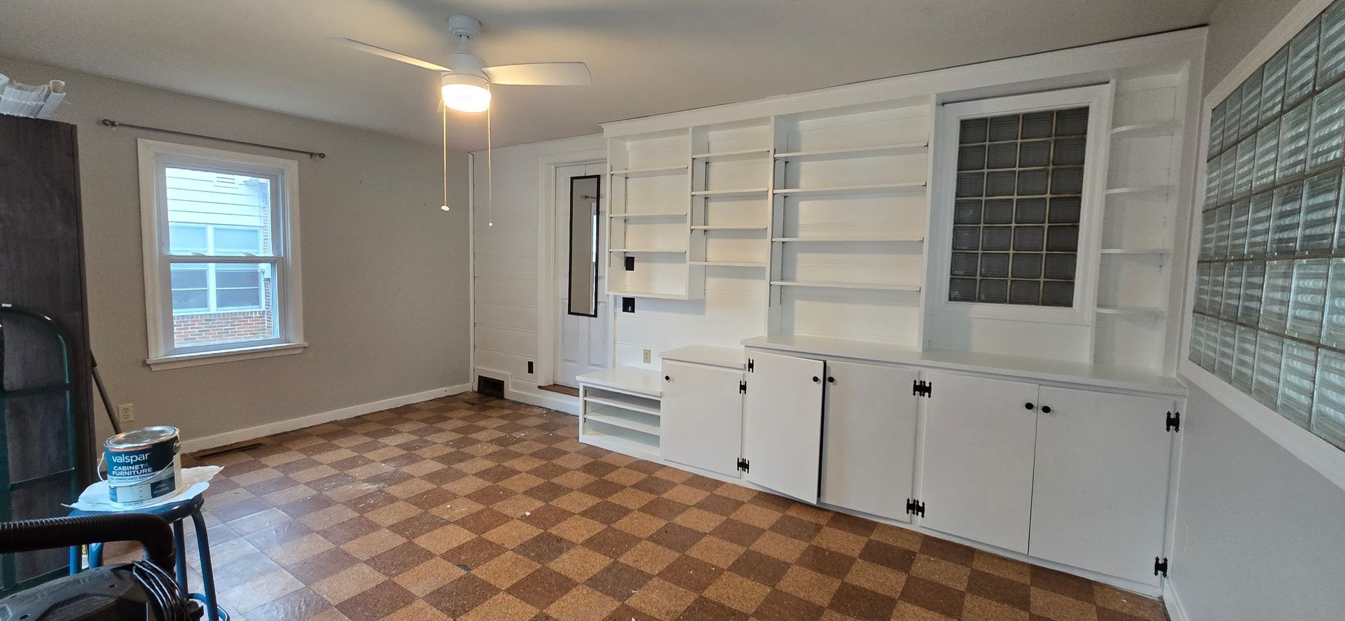 Living room with built-in white shelves, a patterned floor, and a window with a glass block wall.